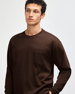 A model wears a brown American Apparel Super Heavyweight T-Shirt with a chest pocket. The image features a logo.
