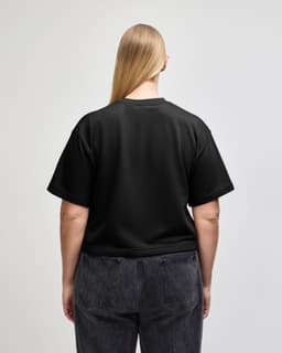 A black mid-length boxy top with short sleeves, displayed from the back on a model wearing light blue jeans.