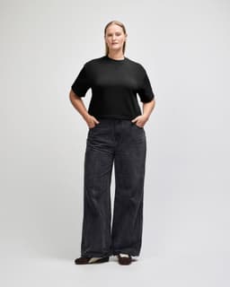 A black mid-length boxy top paired with light blue trousers, worn by a model standing upright. The outfit features a casual style.