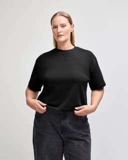 A black mid-length boxy top with short sleeves, styled with light blue jeans. The fabric appears soft and textured.