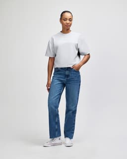 A woman stands in a grey, mid-length boxy top paired with light blue wide-leg jeans, wearing white shoes.