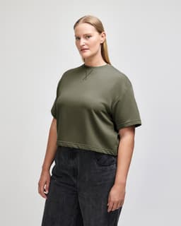 A women's mid-length boxy top in olive green, featuring short sleeves and a relaxed fit, with a logo.
