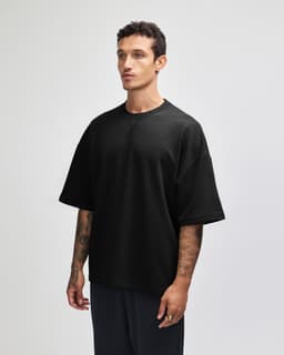 A black oversized boxy top with short sleeves displayed on a model from the side, featuring a logo.