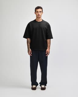 A black oversized boxy top with a crew neckline, featured on a model with short blonde hair.