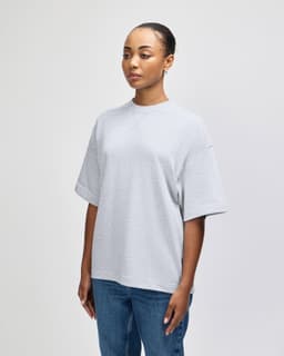 A grey oversized unisex boxy top displayed on a model, showcasing a side profile view. The top features a logo.