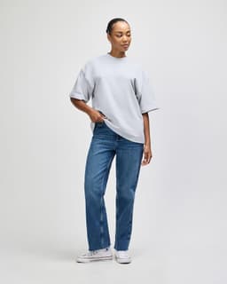 A model wearing a grey oversized boxy top and green cargo pants, with arms raised behind the head.