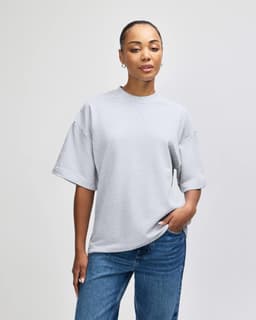 A grey unisex oversized boxy top with a round neckline and short sleeves, featuring a logo.