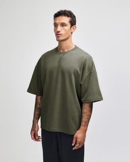 A unisex oversized boxy top in olive green, featuring short sleeves and a casual fit. The shirt has a logo.