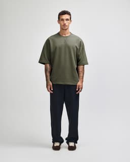A unisex oversized boxy top in olive green, featuring short sleeves and a relaxed fit. Contains a logo.