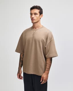 A beige oversized unisex boxy top with short sleeves and a simple design, featuring a logo.