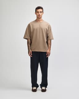 A model wearing a brown oversized boxy top paired with dark pants, standing against a neutral background.