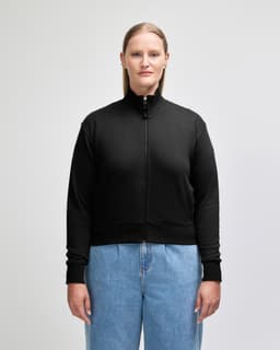 A women's full-zip jacket in black, featuring a high collar and ribbed cuffs, paired with blue jeans.