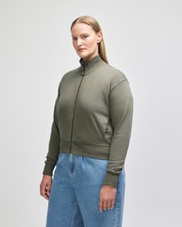 A women’s full-zip jacket in olive green, featuring a high collar and ribbed cuffs, worn over blue jeans.