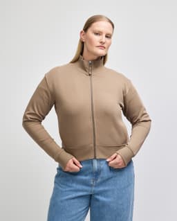 A women's full-zip jacket in a light brown hue, featuring a high collar and ribbed cuffs. There is a logo present.