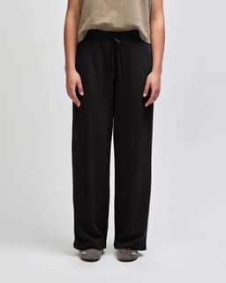 Wide leg pants in black with a drawstring waist, featuring a relaxed fit and pockets. The model is wearing a long-sleeved top.