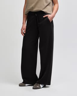 Wide leg pants in black, featuring a drawstring waist and side pockets, showcased from the side view.