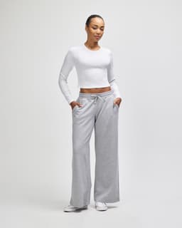 A pair of grey wide leg pants displayed with a model wearing a white long-sleeve top. The pants feature pockets and a drawstring.