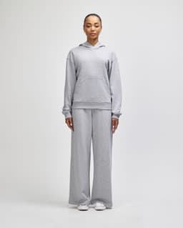 Grey wide-leg pants paired with a matching hoodie, featuring a logo, modelled by a standing woman.