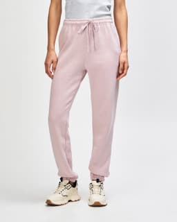 Unisex sweatpants in soft pink, featuring an elastic waistband and cuffs, shown with a pair of sneakers.