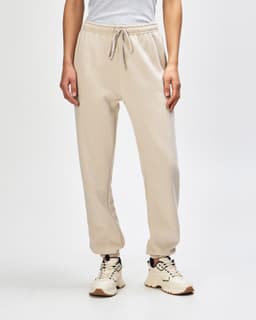 Unisex sweatpants in beige with an elastic waistband and cuffed ankles, paired with a light pink sweat top.