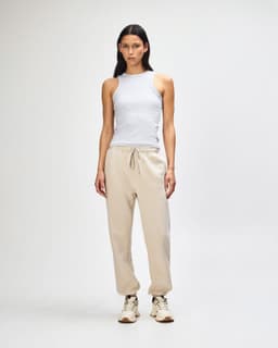 Unisex sweatpants in cream, paired with a pink sweatshirt, worn by a model standing in a neutral background.