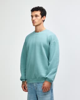 A unisex crewneck sweatshirt in a soft green colour, featuring a relaxed fit and ribbed cuffs. It has a logo.