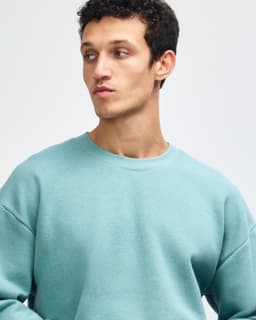 A unisex crewneck sweatshirt in green, featuring a relaxed fit and a simple design. It has a logo on it.