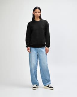 A unisex crewneck sweatshirt in black, paired with light blue cargo pants, featuring curly hair. The sweatshirt has a logo.