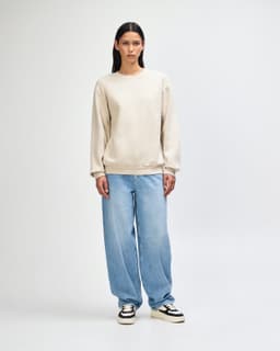 A unisex crewneck sweatshirt in beige worn with light blue jeans and black sneakers, featuring a logo.