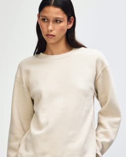 A unisex crewneck sweatshirt in cream with a relaxed fit. It features a subtle logo and soft fleece material.