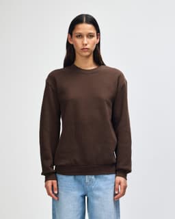 A unisex crewneck sweatshirt in dark brown, featuring long sleeves and a casual fit. The garment has a logo.