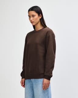 A unisex crewneck sweatshirt in brown, featuring a side view with a model wearing it, showcasing its relaxed fit.