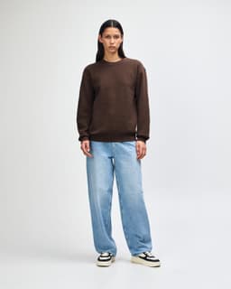 A unisex crewneck sweatshirt in brown worn with light blue cargo pants, featuring a simple design and a logo.