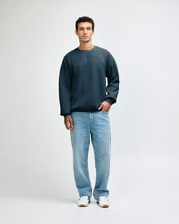 A unisex crewneck sweatshirt in a deep teal colour, paired with light blue cargo pants and styled on a model.