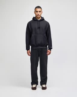 A black pullover hooded sweatshirt worn with matching dark trousers, featuring a logo on the sleeve.