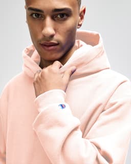 A model wearing a pink Champion Reverse Weave® adult pullover hooded sweatshirt with a visible logo on the sleeve.