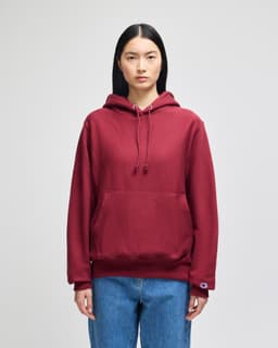 A maroon pullover hooded sweatshirt with a front pocket and a logo on the sleeve. Suitable for casual wear.