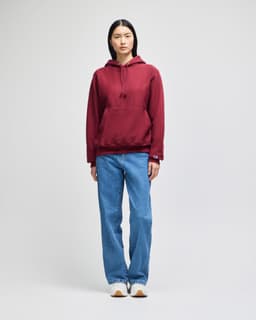 A model wearing a burgundy pullover hooded sweatshirt paired with light blue jeans, featuring a logo.