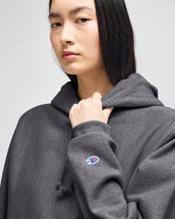 A dark grey pullover hooded sweatshirt with a logo on the sleeve, featuring a relaxed fit and drawstring hood.