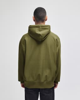 An olive green hooded sweatshirt with a large back pocket and a drawstring hood. The model is facing away from the camera.