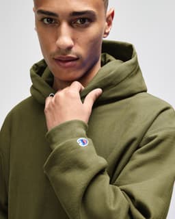 A man in a green hooded sweatshirt, featuring a logo on the sleeve and a focused expression.