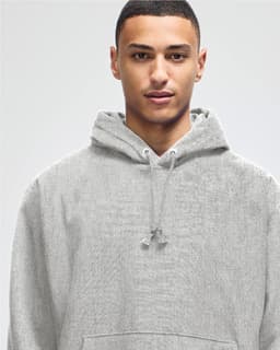 A grey hooded sweatshirt with a drawstring hood, featuring a logo. The model has short dark hair.