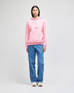 A pink pullover hooded sweatshirt, featuring a front pocket and a logo, worn with blue jeans.