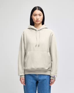A light grey pullover hooded sweatshirt with a front pocket and a logo on the sleeve, worn by a model.