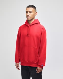 A red pullover hooded sweatshirt with a front pocket and logo on the sleeve, displayed on a model.