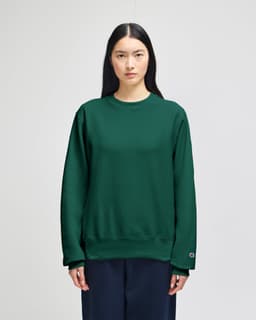 A green Champion Reverse Weave® adult crew sweatshirt displayed on a model, featuring a logo on the sleeve.