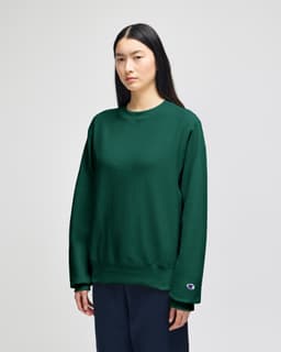 A green Champion Reverse Weave® adult crew sweatshirt displayed on a model, featuring a logo on the sleeve.