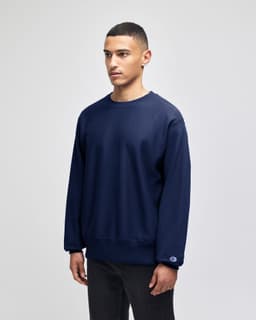 A navy blue Champion Reverse Weave® adult crew sweatshirt with a logo on the cuff, displayed on a model.