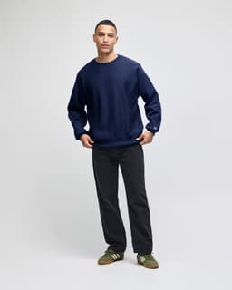 A navy blue sweatshirt with a crew neck and long sleeves, styled with dark pants and green shoes. The sweatshirt features a logo.