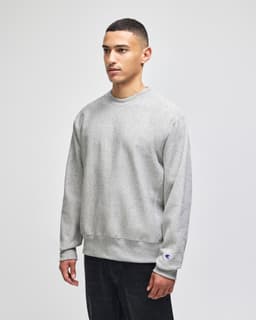 A grey Champion Reverse Weave® adult crew sweatshirt with a logo, modelled by a person.